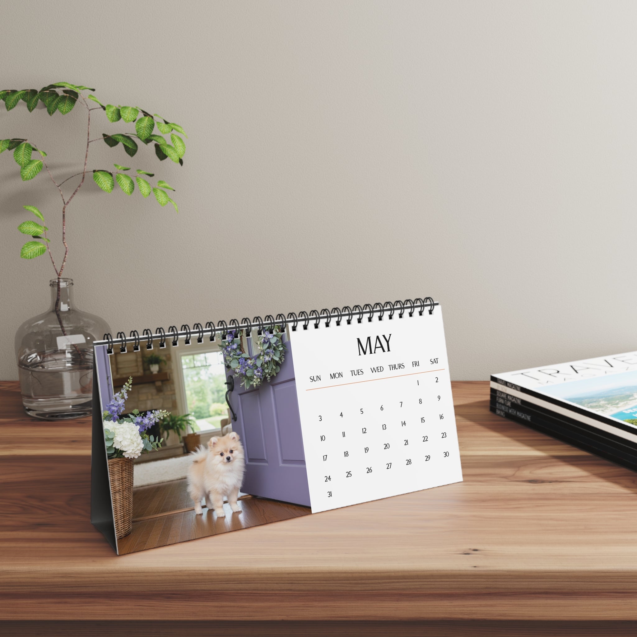 Calendar on a wooden surface with a decorative plant and another calendar in the background.