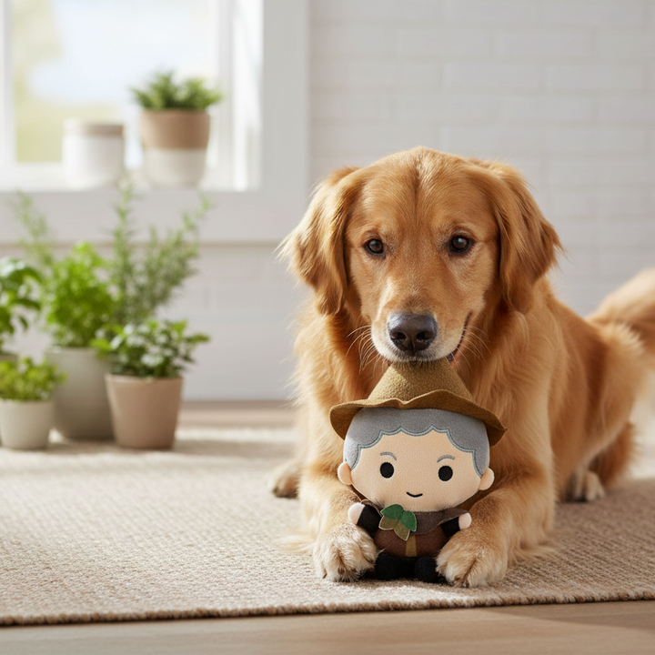 A golden retriever dog lies on a beige rug in a bright room, holding a small Professor Sprout plush character toy in its mouth. Several potted green plants sit near a window in the background.